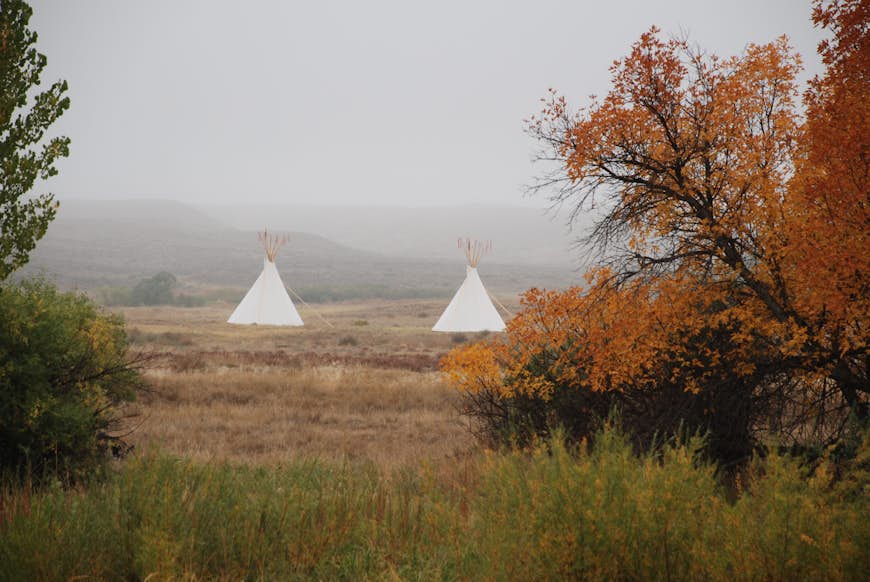 Tipis across the Laramie River at Fort Laramie National Historic Site with beautiful fall foliage in the foreground and fog in the background.