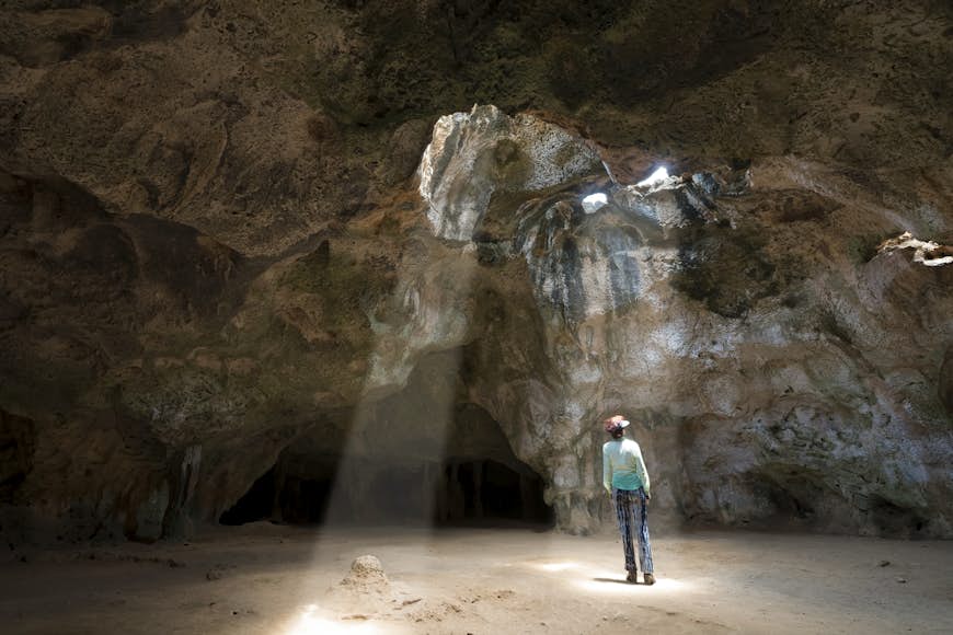 A woman stands in a shaft of light that is coming through a gap in the roof of a cave