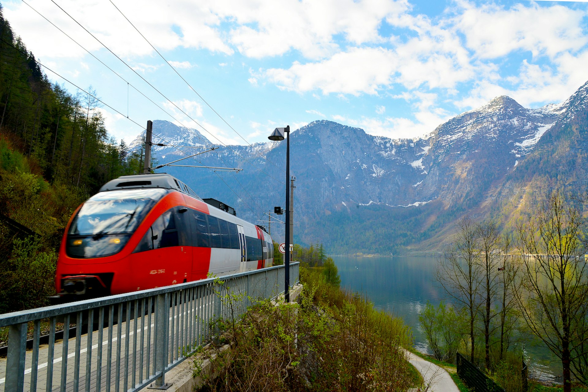 A high-speed train passing the Hallstatt station with mountains in the distance, Austria