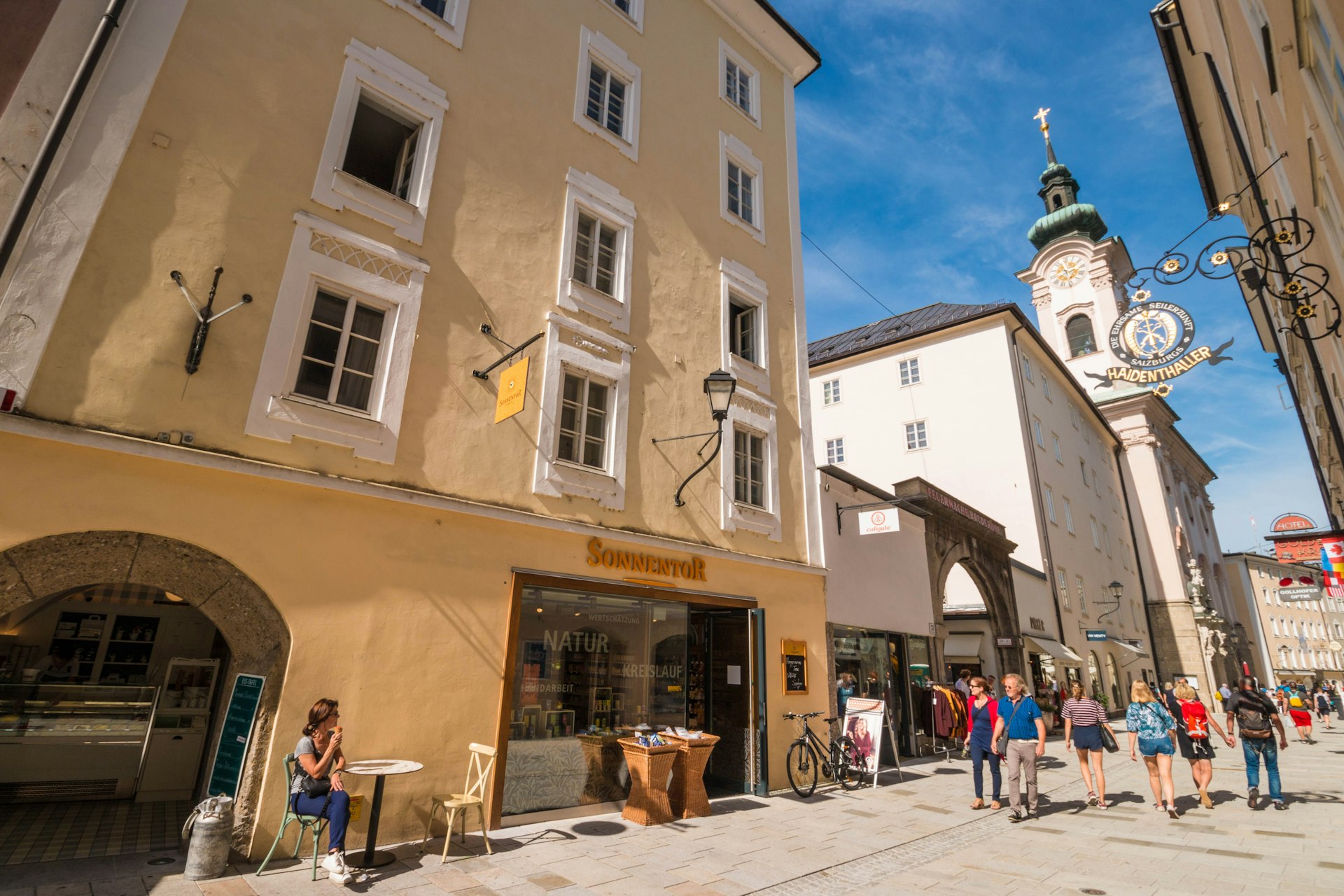 People walking down a pedestrianised street in a city with a baroque church in the backgroun