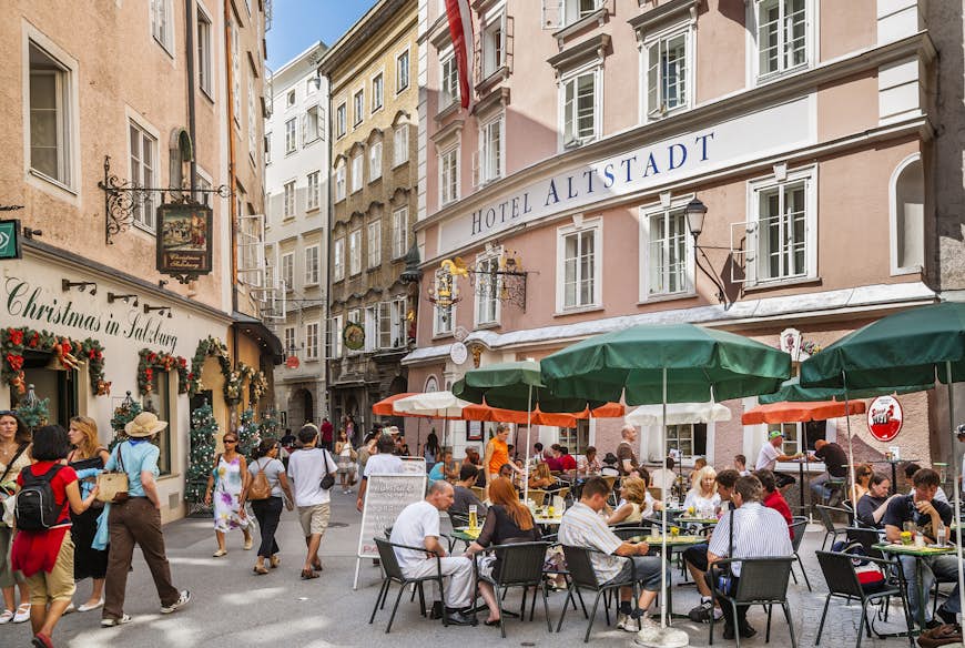 Les gens s'assoient à des tables à manger en plein air dans une rue piétonne de la vieille ville de Salzbourg