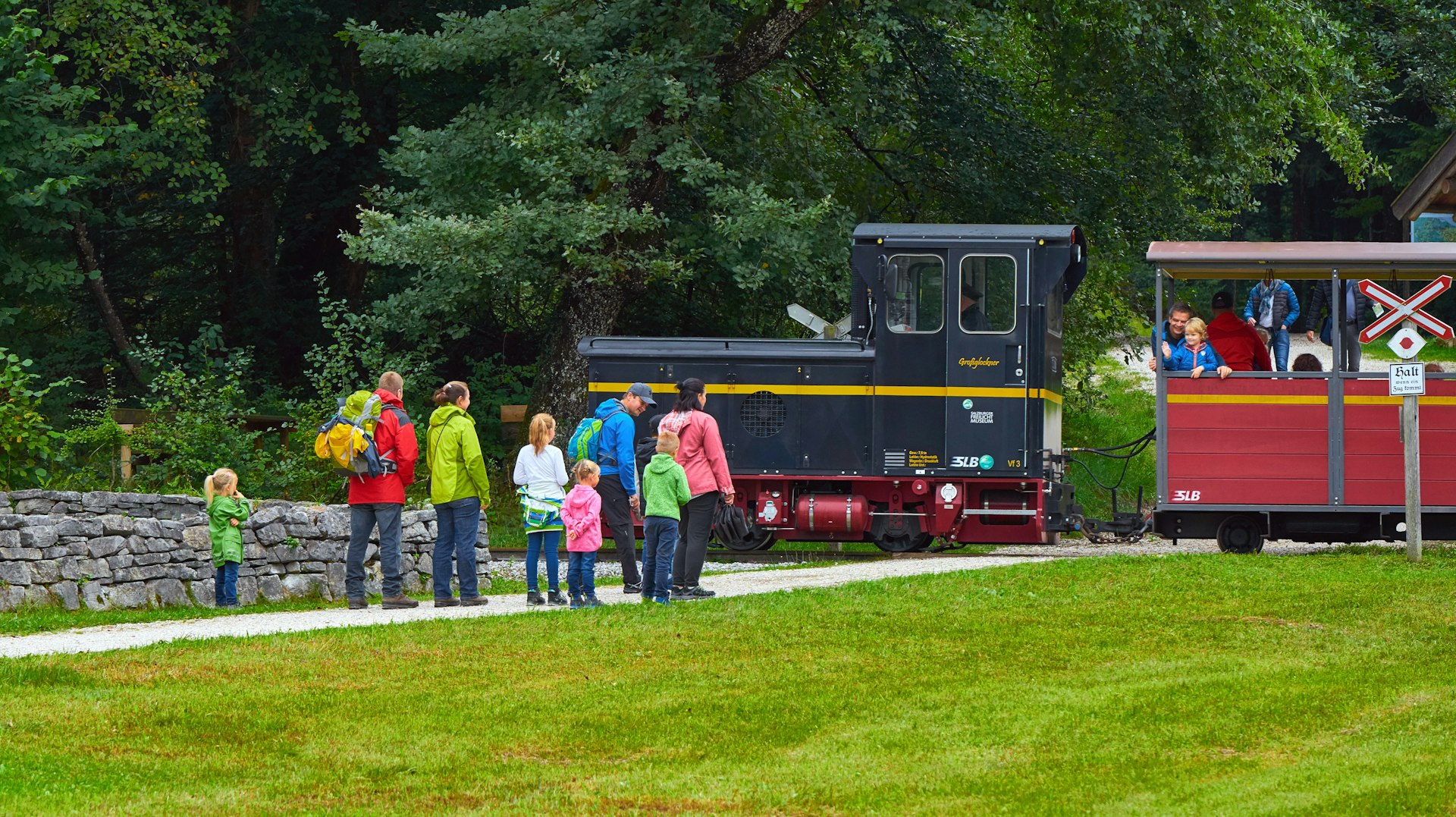 A line of young children waiting with adults to go on a small steam train