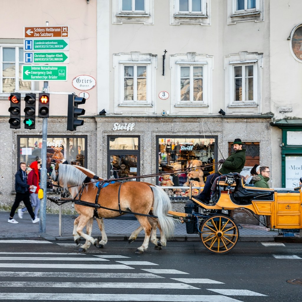 Salzburg, Austria - November 1, 2019: Coachman rode touring carriage with passengers running through crosswalk at junction with traffic lights inside old town.; Shutterstock ID 2147339837; your: Brian Healy; gl: 65050; netsuite: Lonely Planet Online Editorial; full: Getting around Salzburg