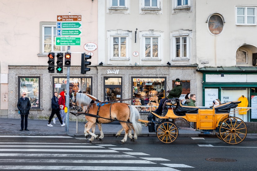 Salzburg, Austria - November 1, 2019: Coachman rode touring carriage with passengers running through crosswalk at junction with traffic lights inside old town.; Shutterstock ID 2147339837; your: Brian Healy; gl: 65050; netsuite: Lonely Planet Online Editorial; full: Getting around Salzburg