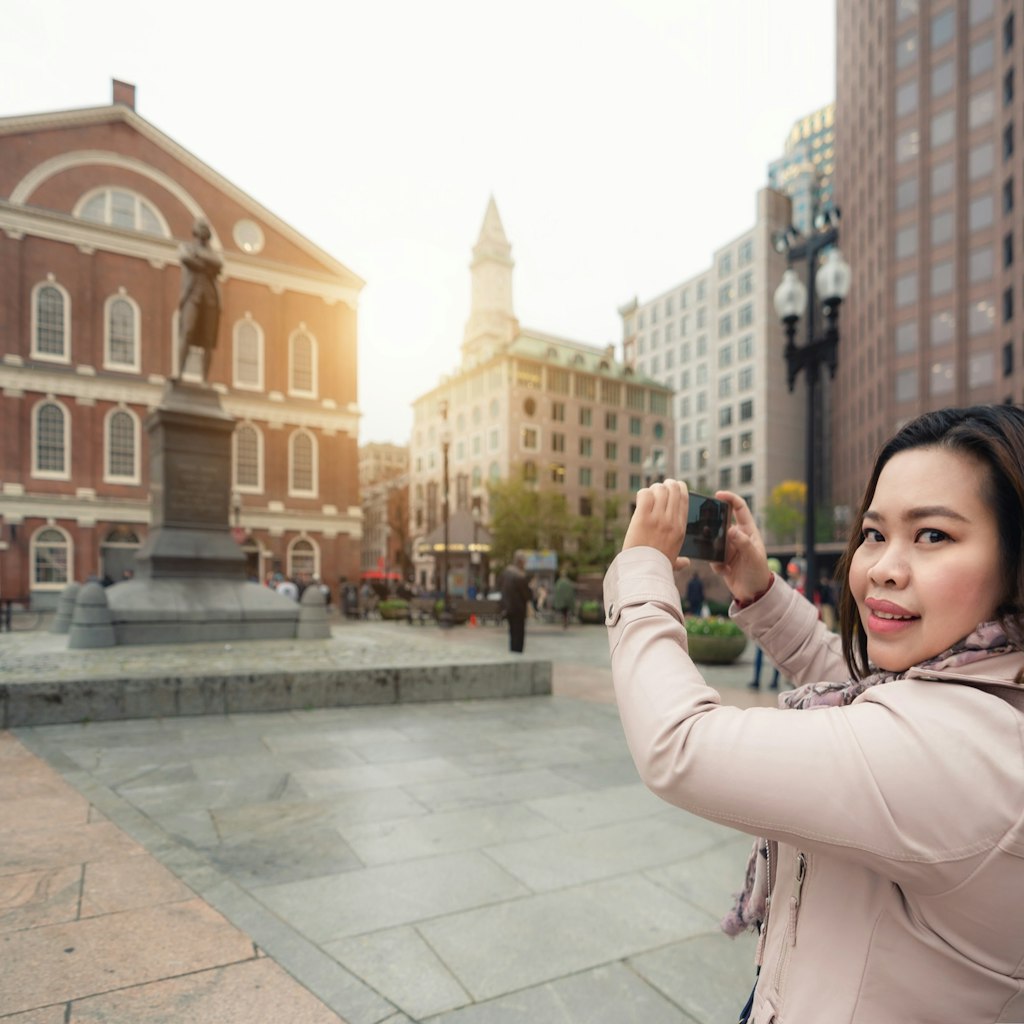 A woman holds up her phone as she takes a photo of Boston landmark. 