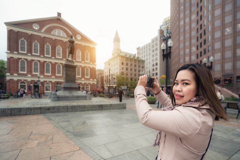 A woman holds up her phone as she takes a photo of Boston landmark. 