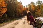 Young woman hanging out of a car window in front of fall trees in Quebec