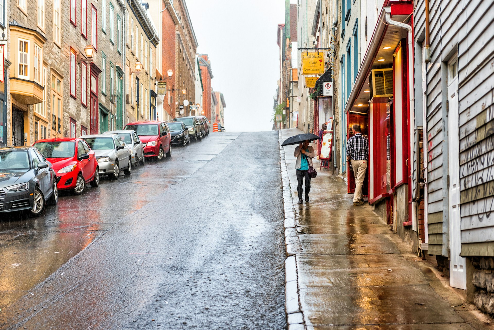 A woman walks with an umbrella by shops down a steep street in the Old Town during heavy rain, Québec City, Québec, Canada