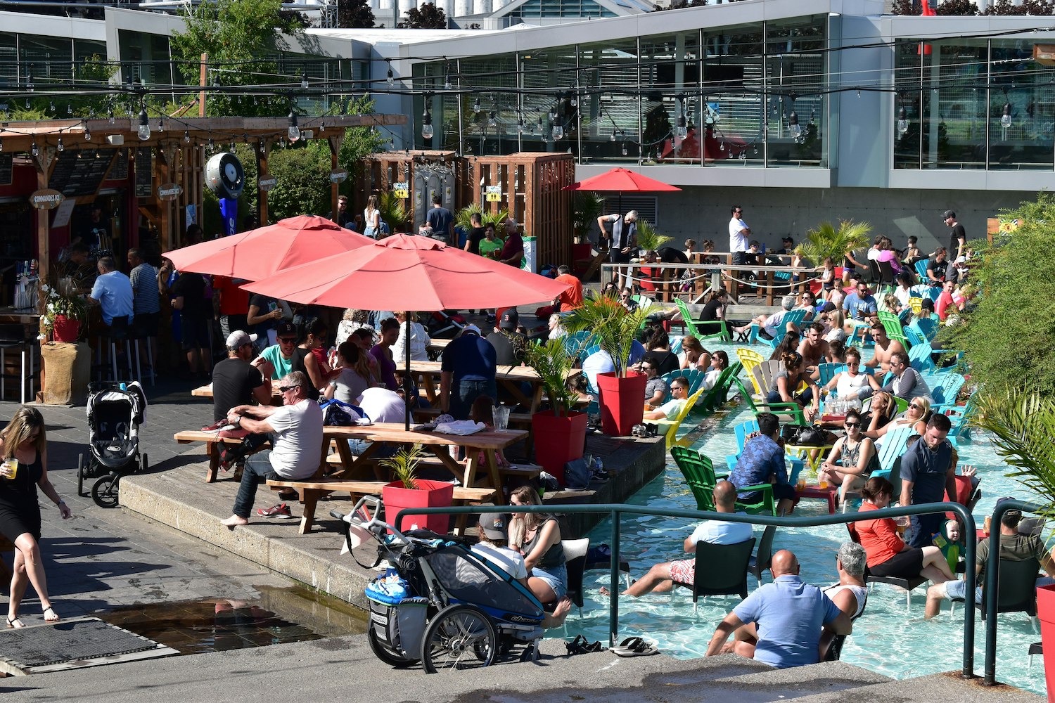 A crowd of people sit at picnic tables and chairs in the wading pools at la Cour arrière du Festibière, Québec City, Québec, Canada