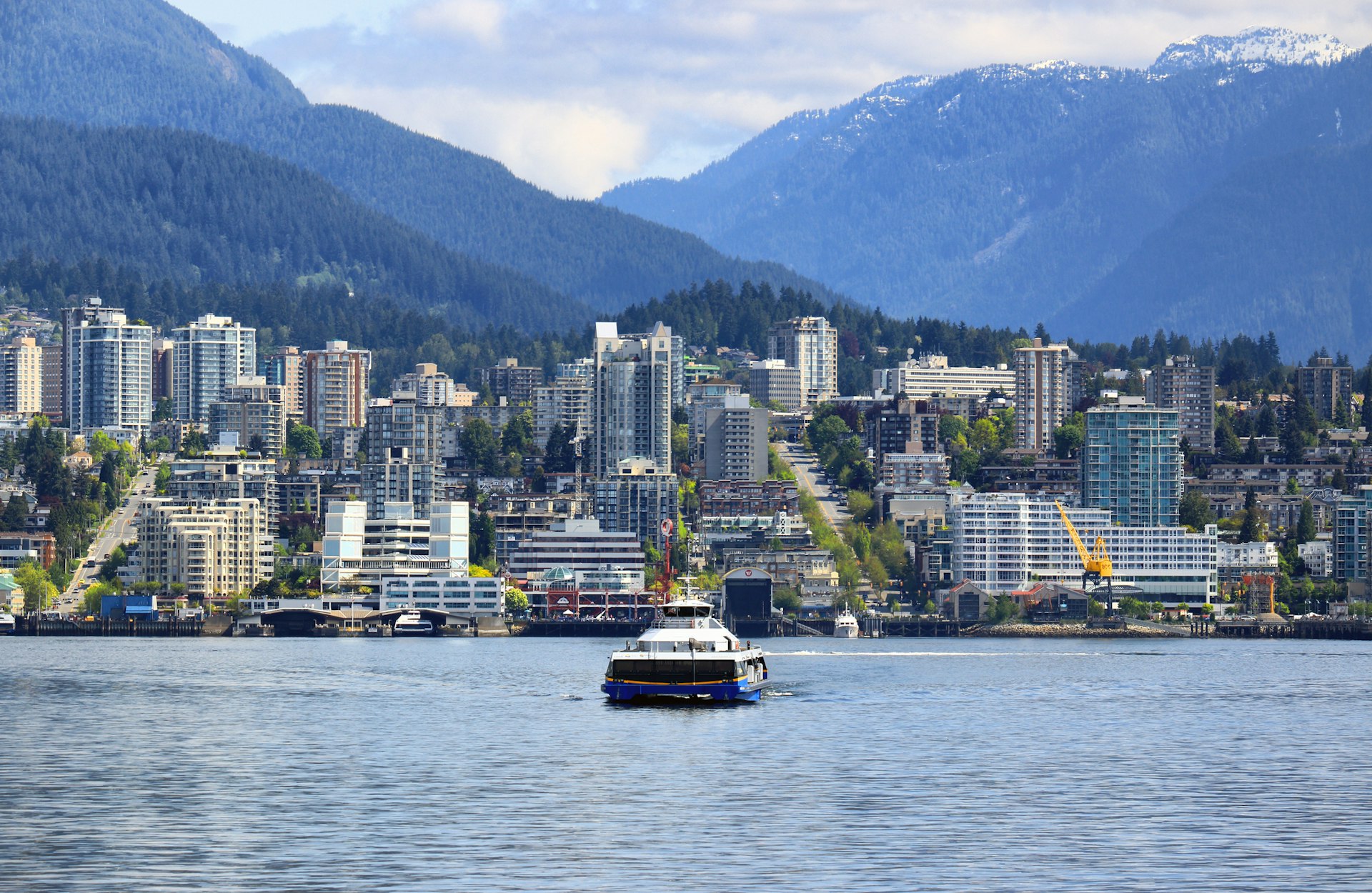 A small ferry heads towards a dockyard with high-rise buildings all around