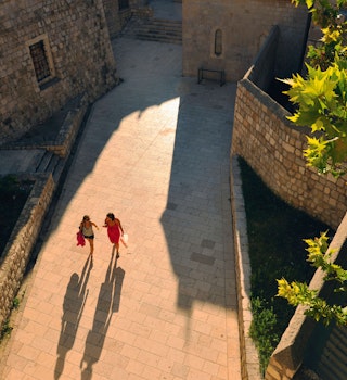 Two people walking through Dubrovnik and casting long shadows, seen from above