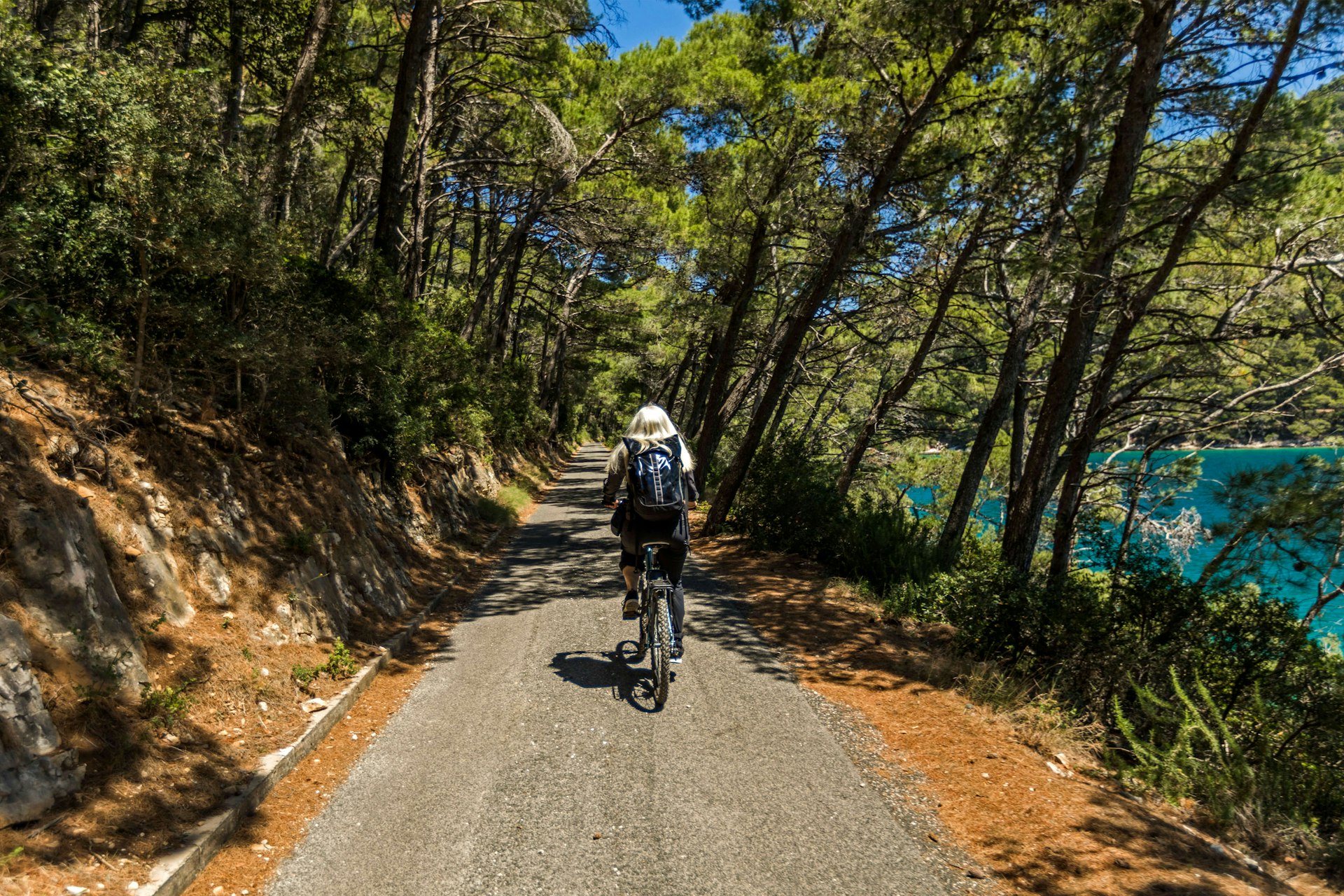 Gray-haired Caucasian woman riding a bicycle on a path near a wooded lake