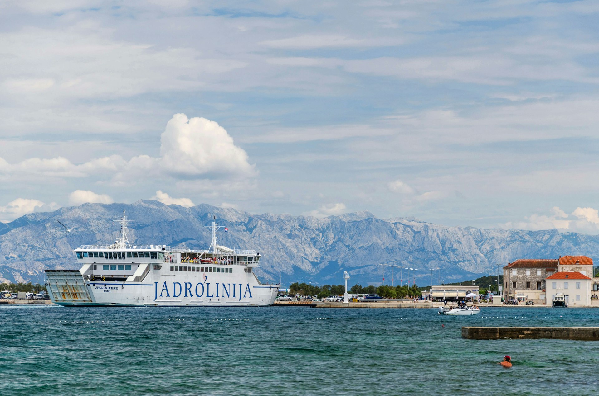 Picturesque view of Jadrolinija ferry against a mountain backdrop on a sunny day