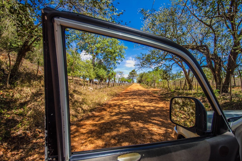 A dusty lane is seen through an open window of a car in the Dominican Republic. 