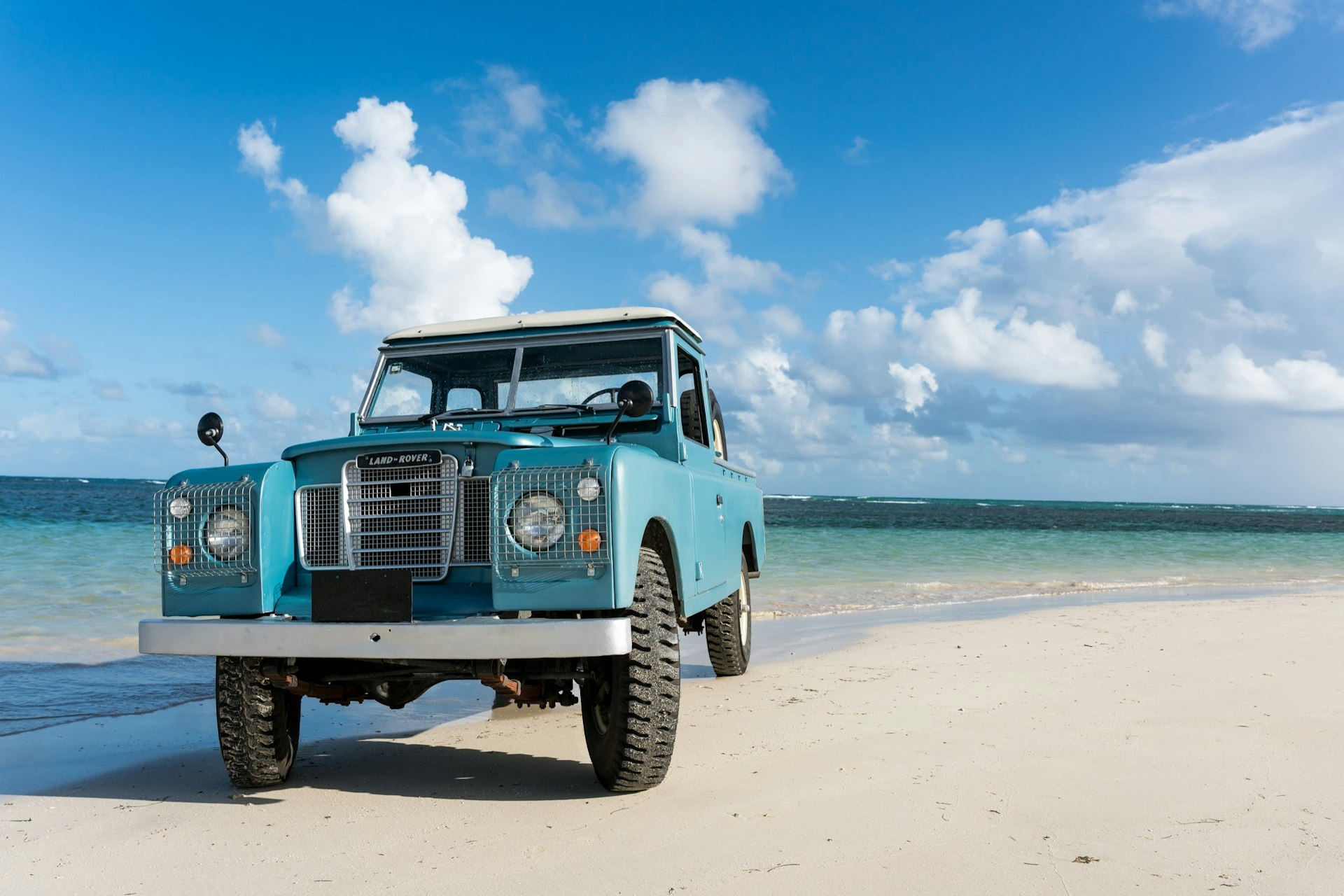 An old blue rover is parked on a beach near the water in Las Terranes, Dominican Republic.