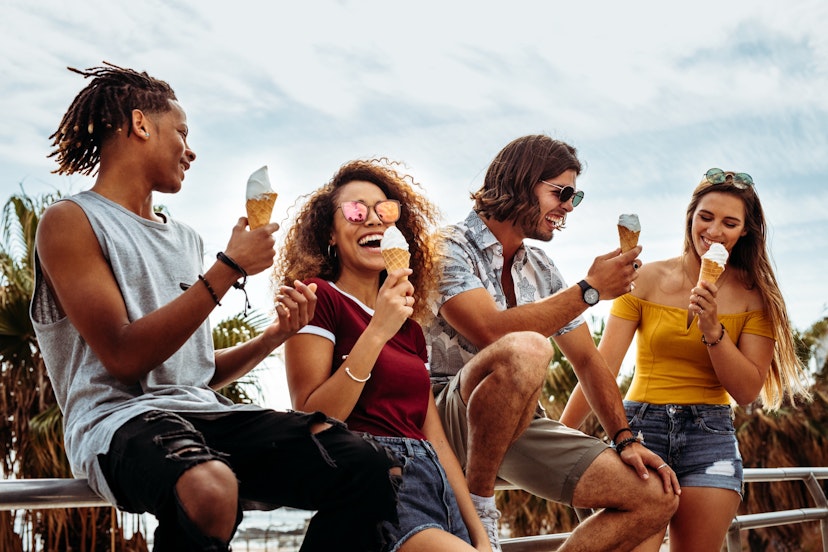 A group of people lean on a railing eating ice cream. 