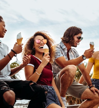 A group of people lean on a railing eating ice cream. 