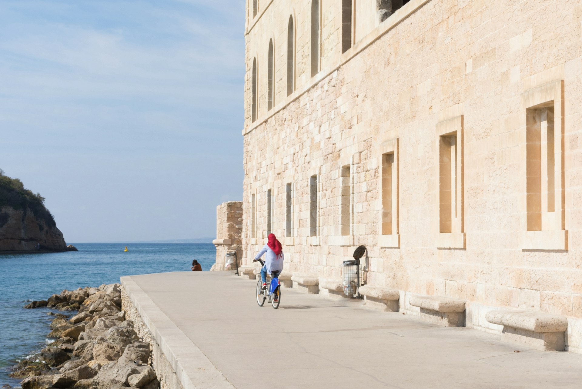 A woman wearing a hijab bicycling on a pathway next to the Mediterranean Sea, Marseille, Bouches-du-Rhône, France