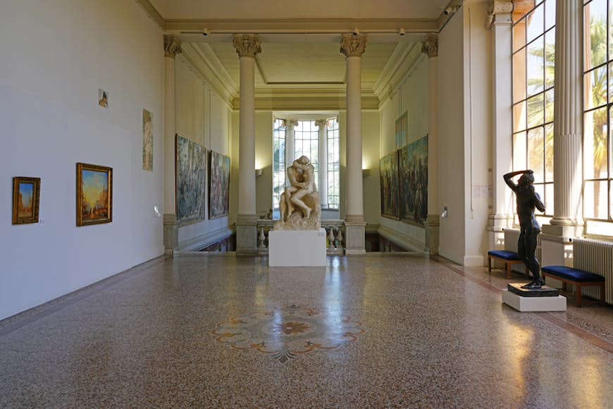 Внутренний коридор художественной галереи с большой статуей двух целующихся людей в конце зала.