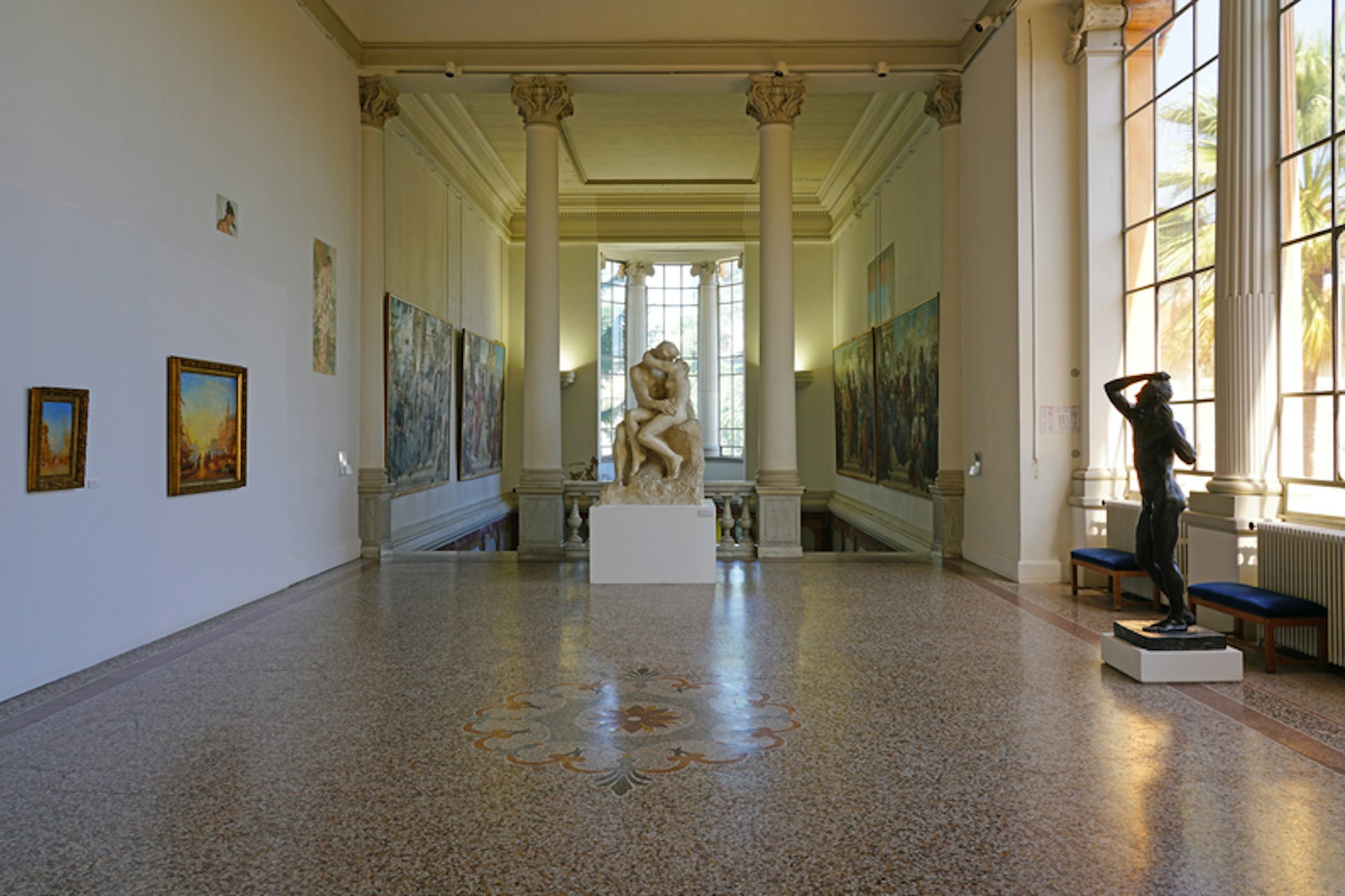 The interior corridor of an art gallery with a large sculpture of two people kissing at the end of the hallway