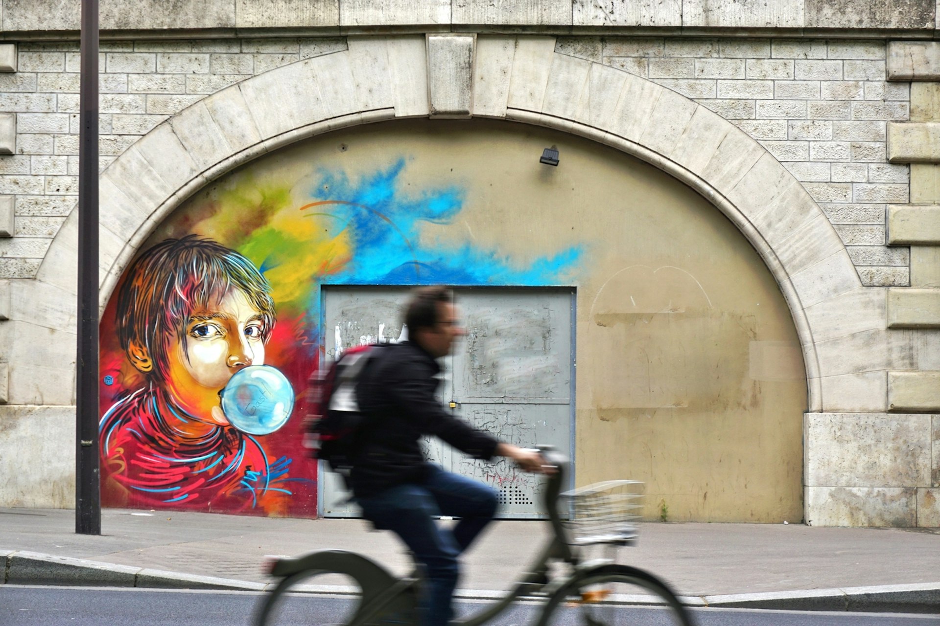 A cyclist speeds by some colourful street art of a woman blowing a bubble