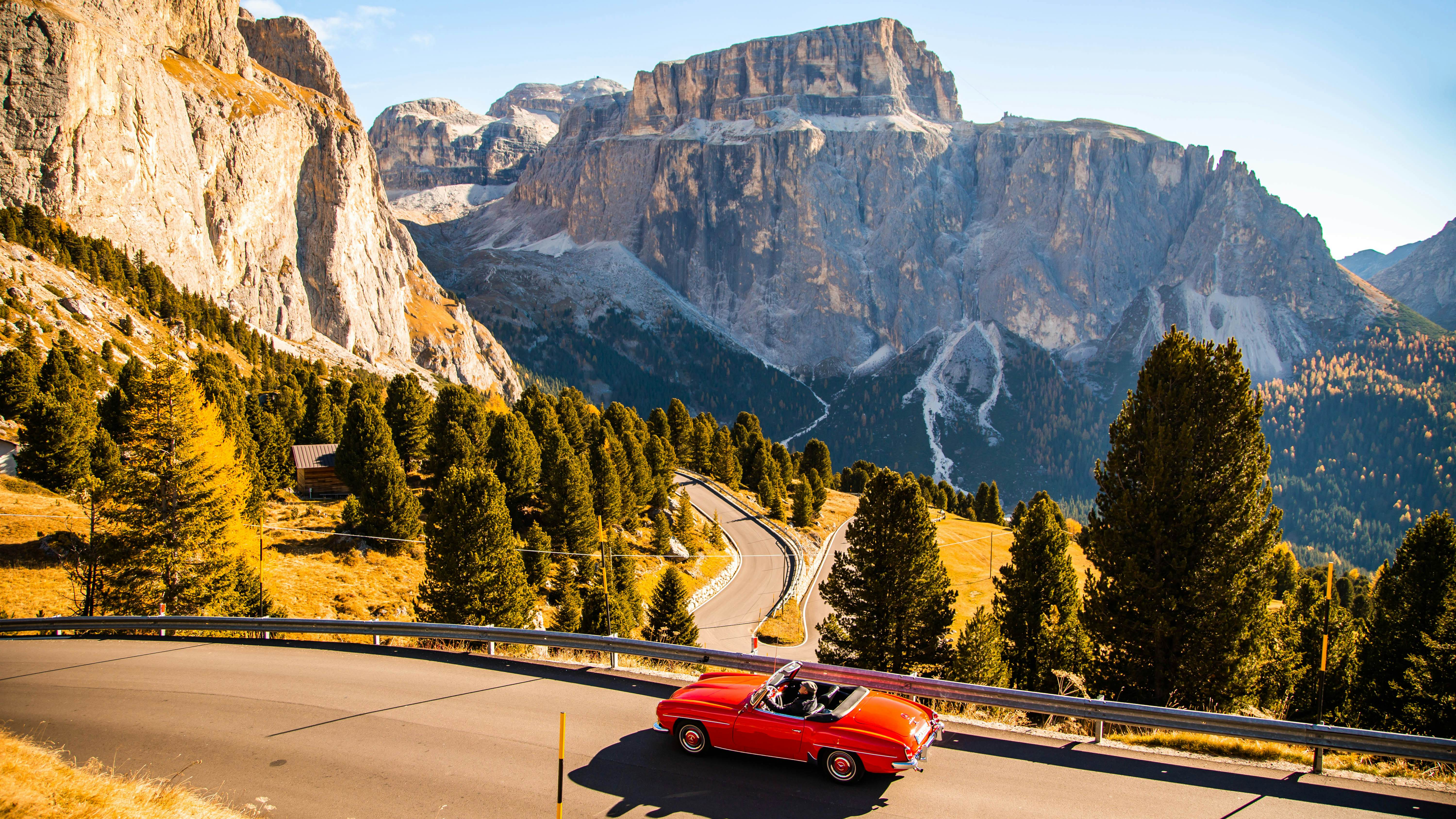Driving with red convertible car in the Dolomites mountains during autumn season