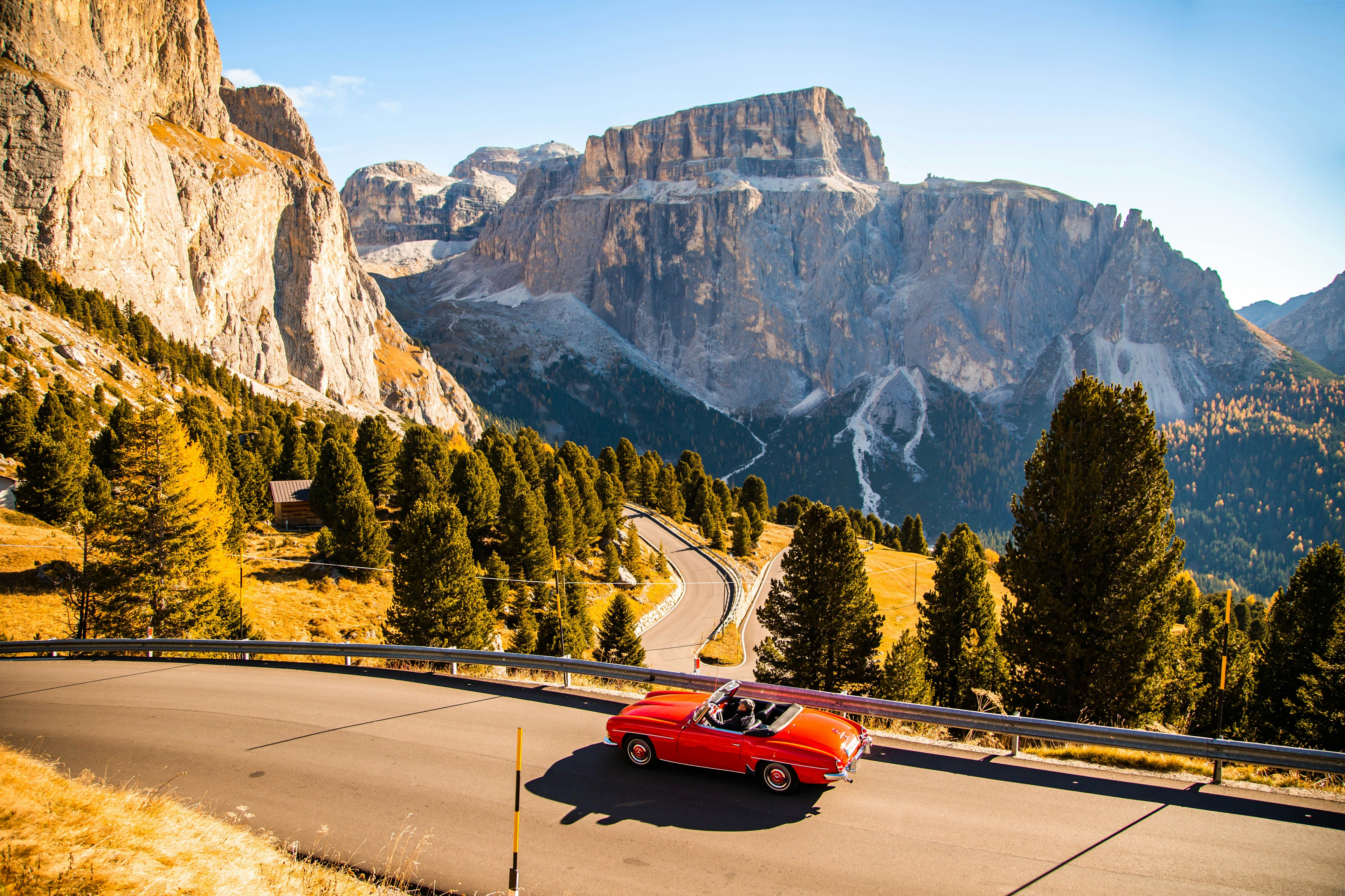Driving with red convertible car in the Dolomites mountains during autumn season