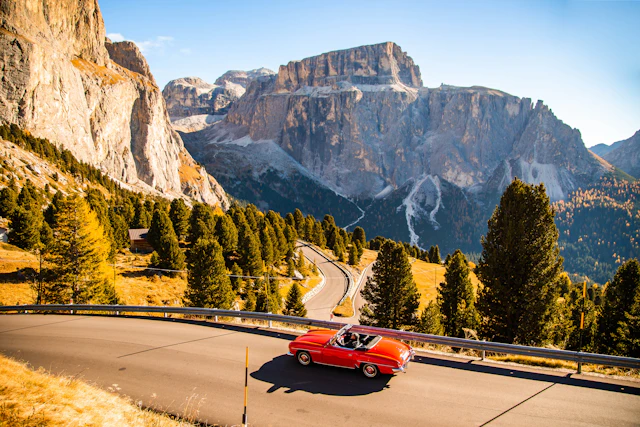 Driving with red convertible car in the Dolomites mountains during autumn season