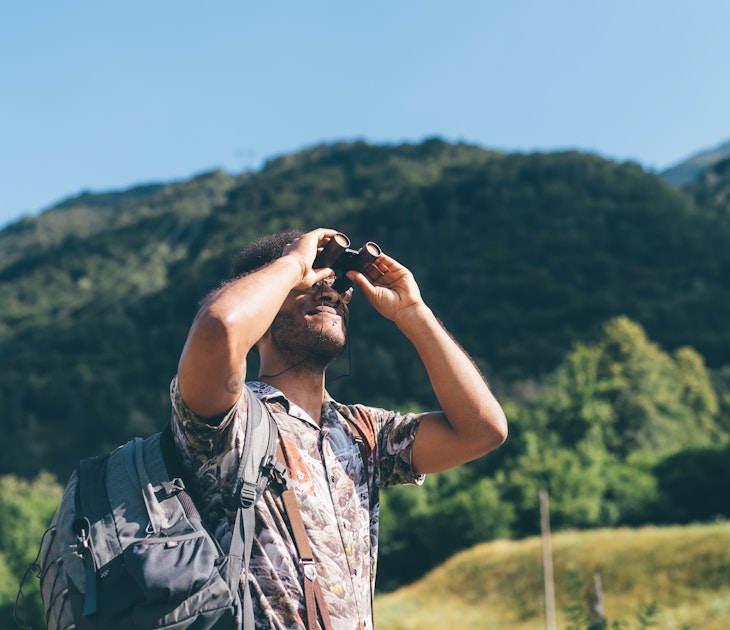 Young male hiker looking up through binoculars, Primaluna, Trentino-Alto Adige, Italy