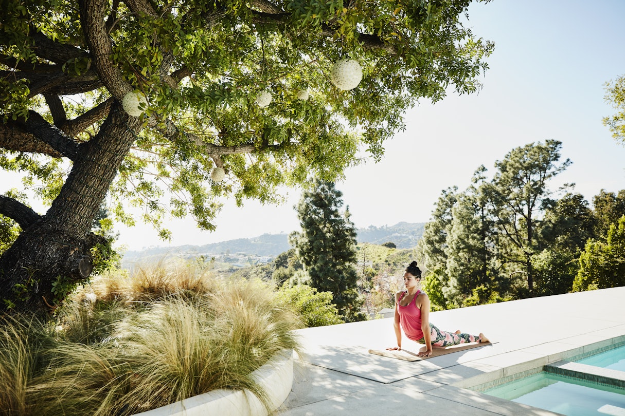 Woman performing yoga on pool deck of home