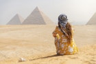 A female tourist sitting on a sand dune and looking at the Pyramids of Giza.