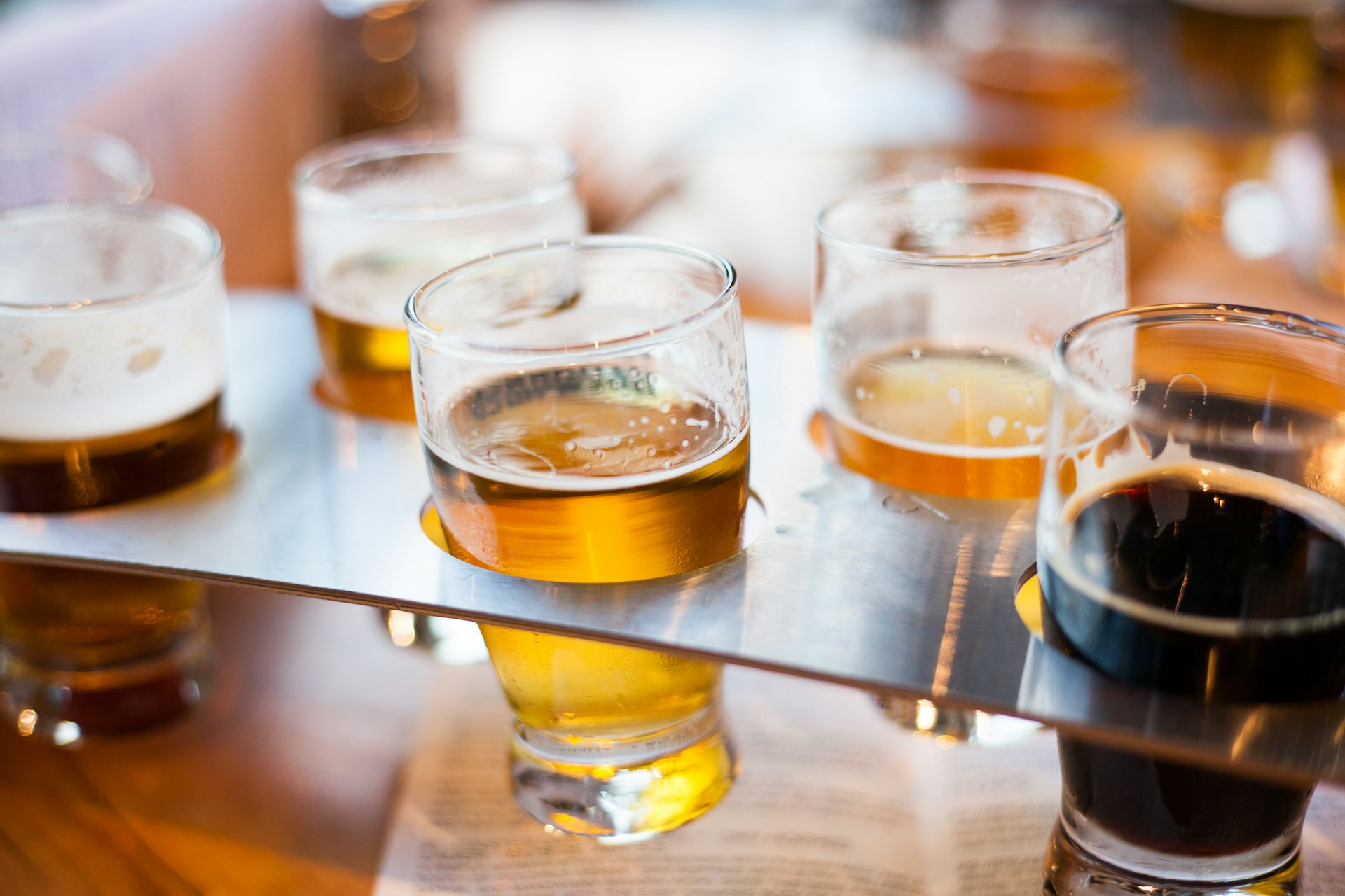 A close up of various types of beer in small glasses held by a metal flight.