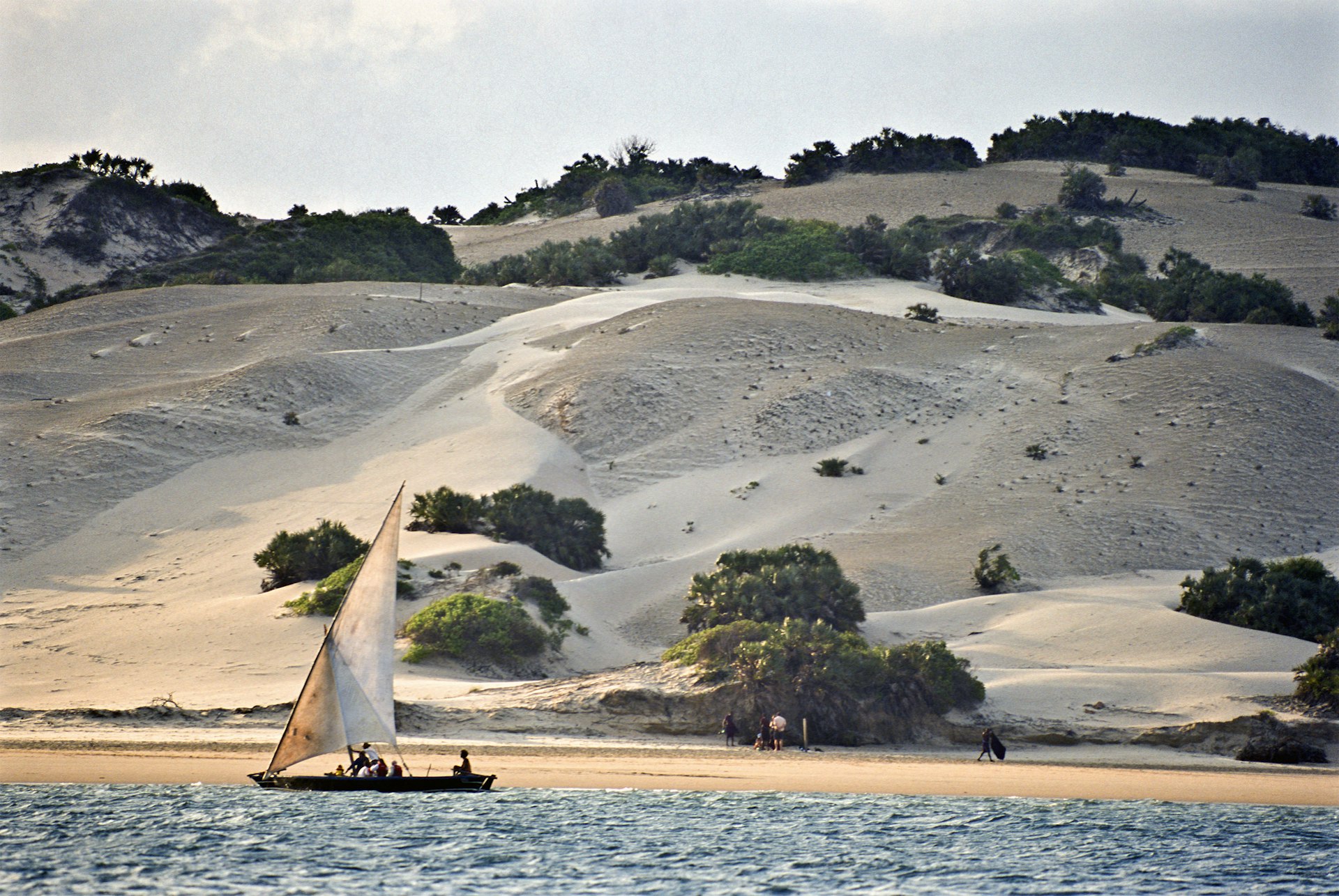 A traditional sailing boat passes vast sand dunes