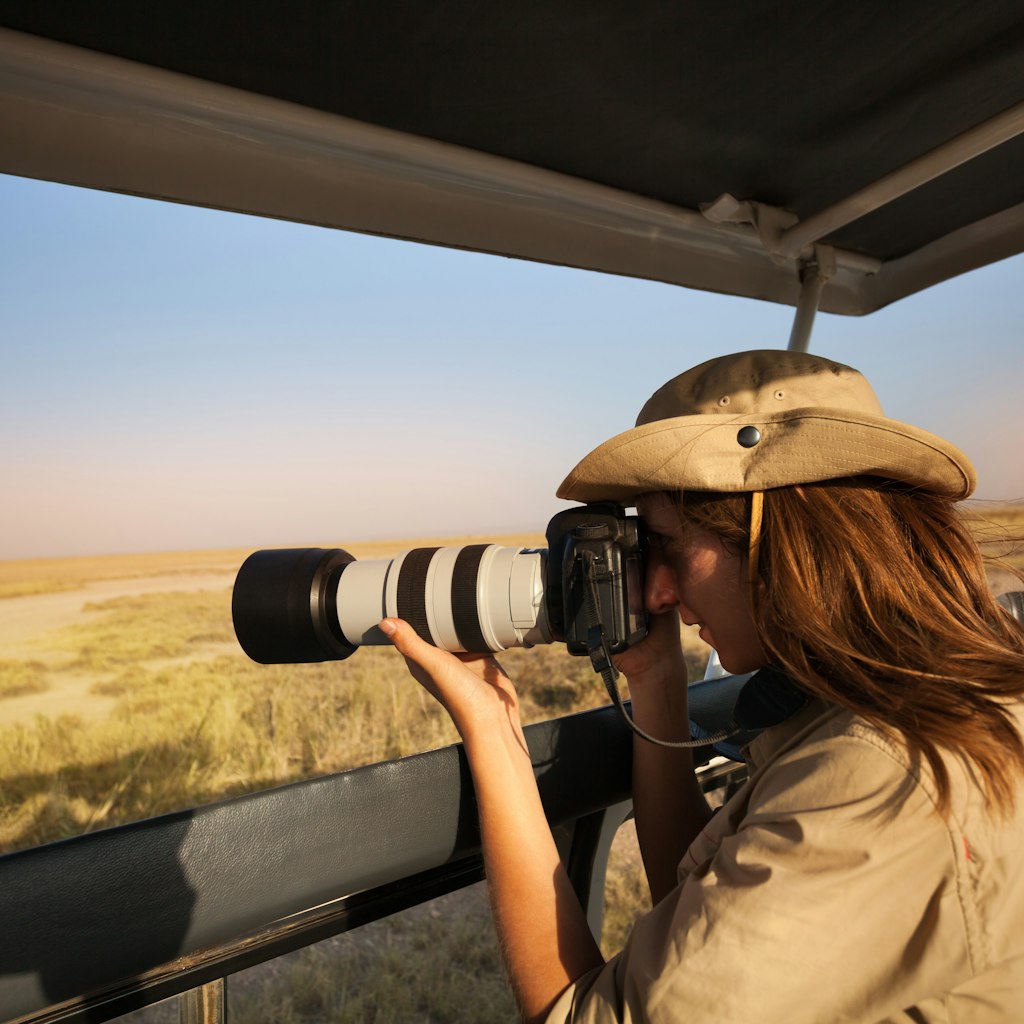 Woman tourist taking photo of savannah with professional camera aboard safari jeep in Africa