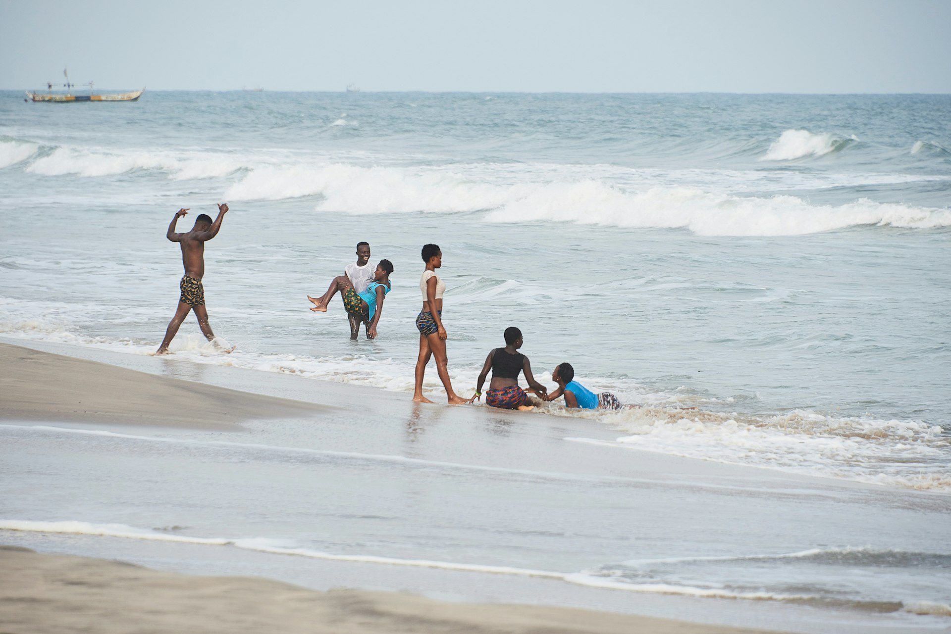 A group of young people splash in the water of the Atlantic Ocean at Kokrobite Beach, Accra, Ghana