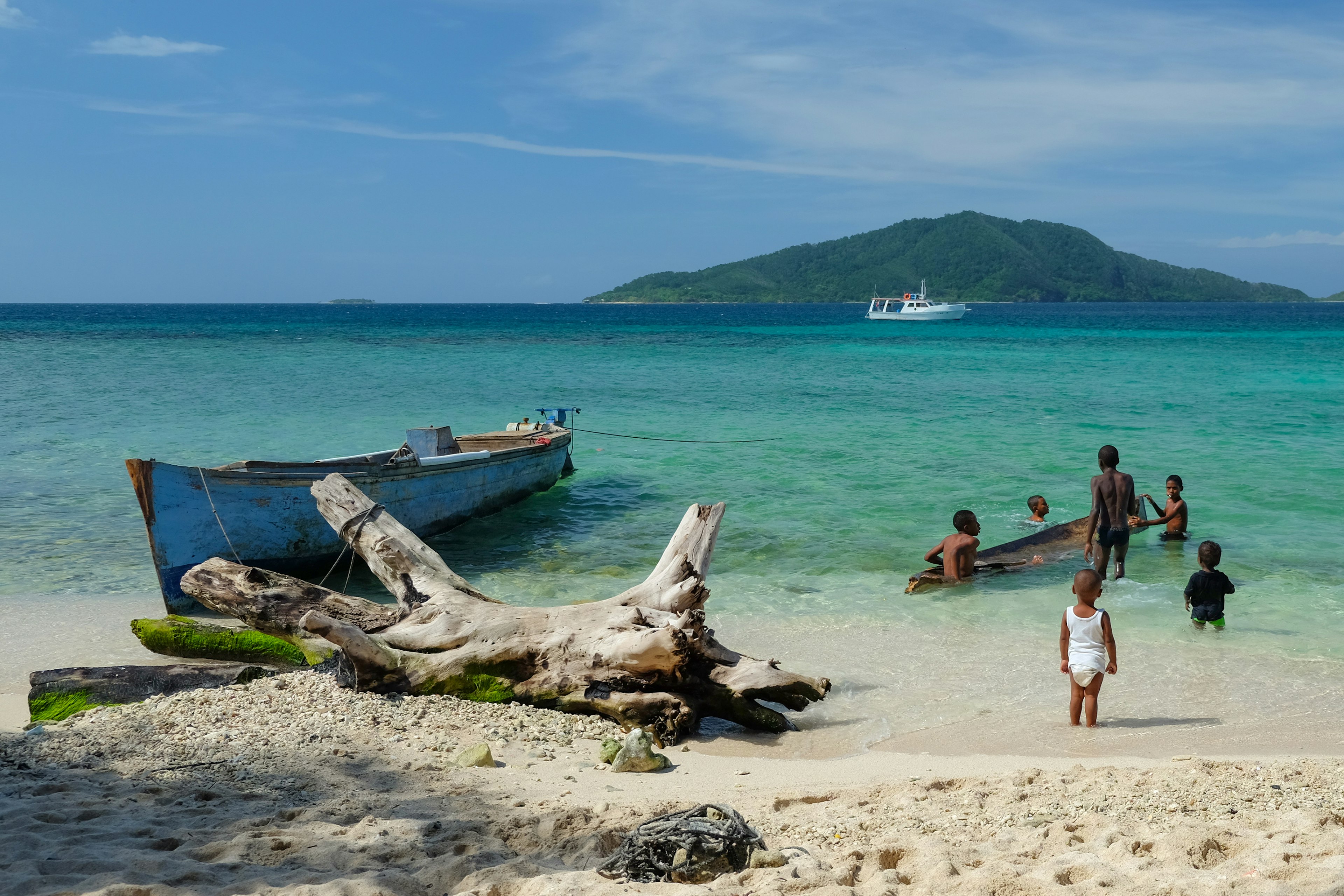 Children playing at the beach next to wooden boats on the Cayos Cochinos, Honduras