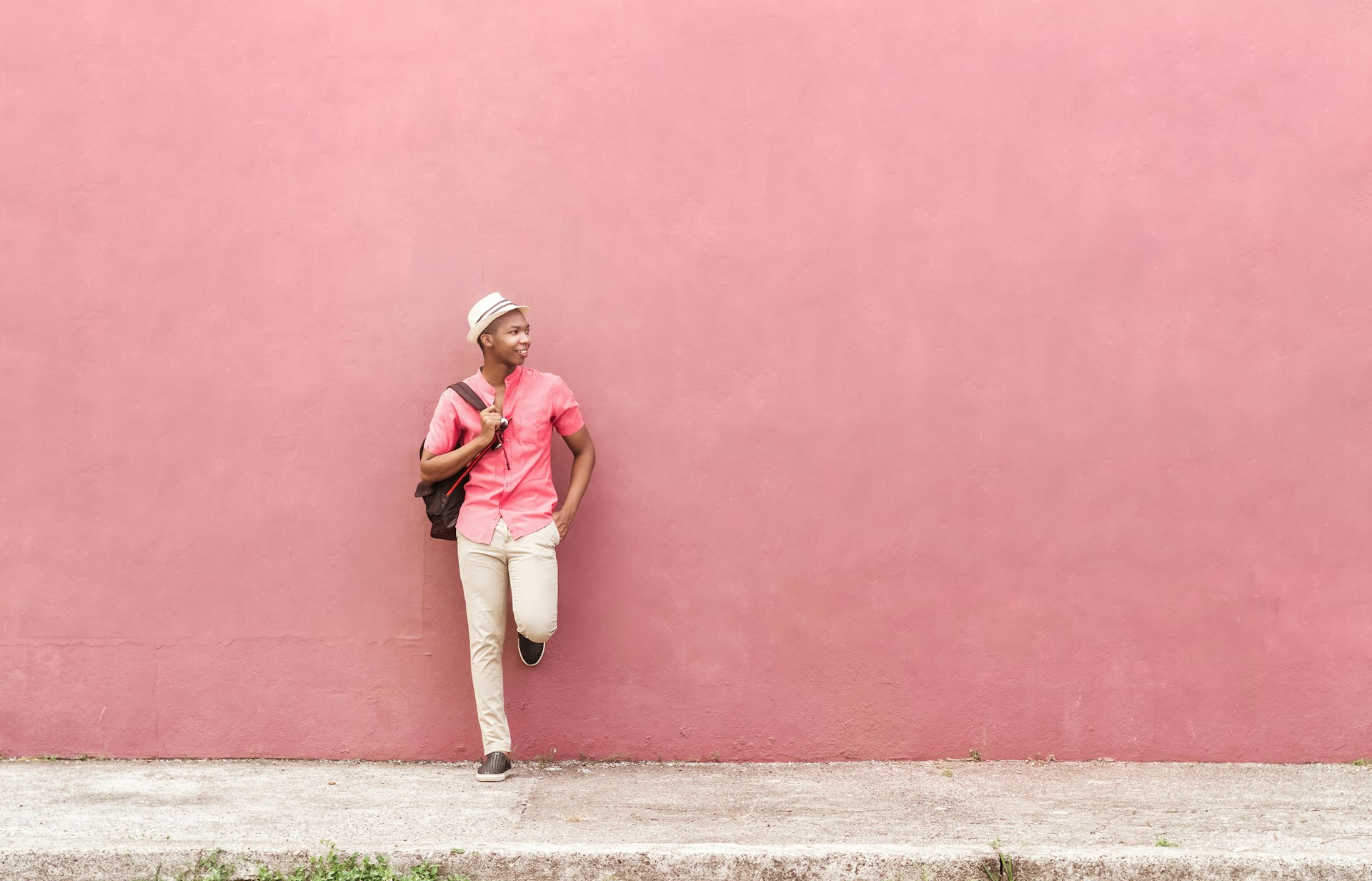 Black man with backpack and white hat stand in front of a colorful pink wall in Honduras