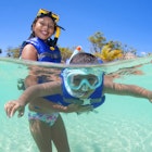 Young girl holding her brother in surface and helping him snorkelling.