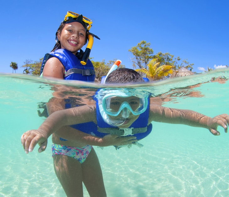 Young girl holding her brother in surface and helping him snorkelling.