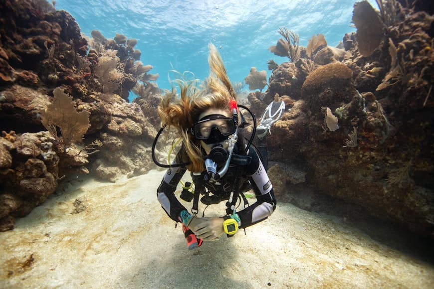 Una mujer con cabello rubio se sumerge entre formaciones de coral frente a Utila, Islas de la Bahía, Honduras, América Central
