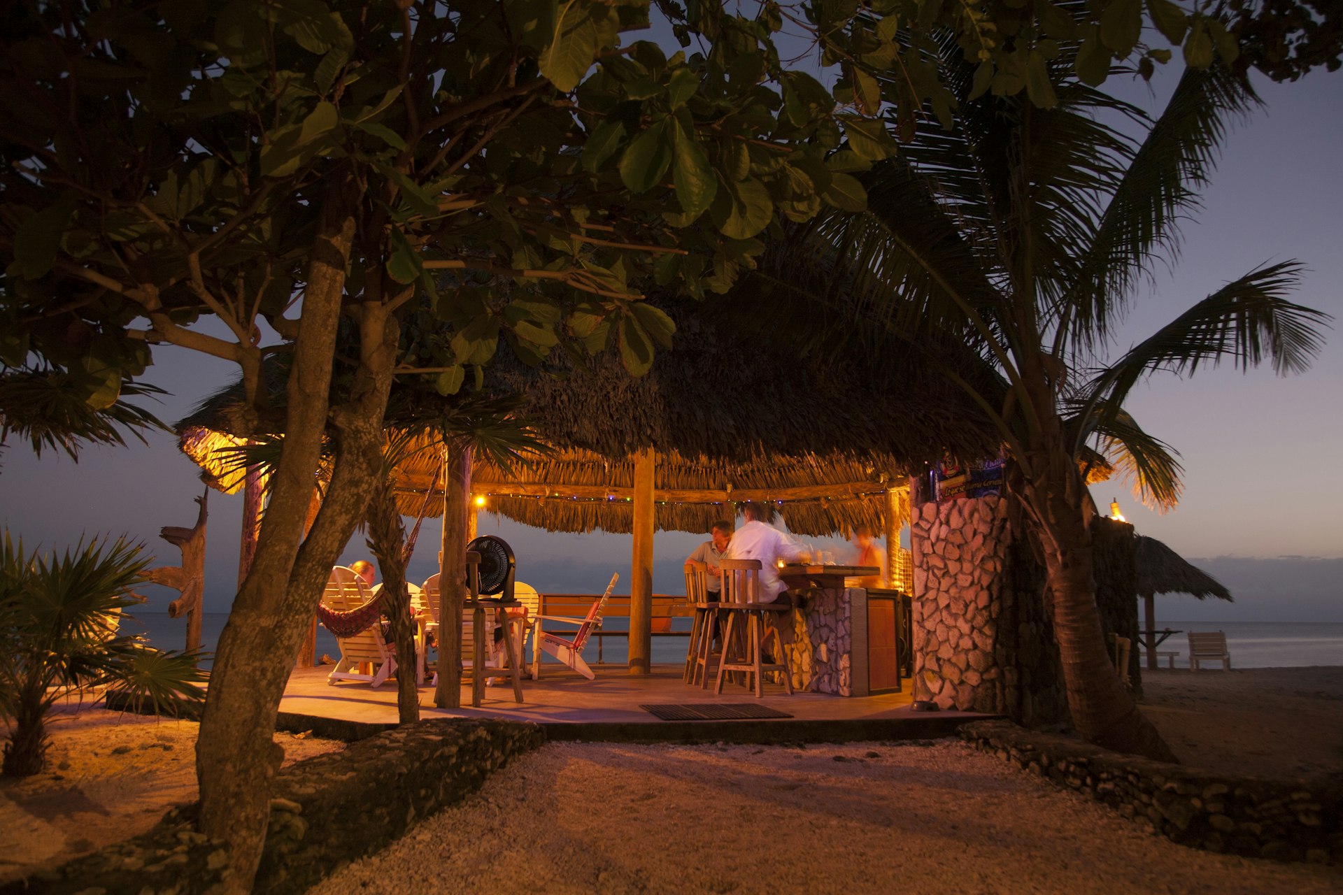 People at a beachside bar in a thatched-roof palapa hut at sunset on Utila, Honduras 