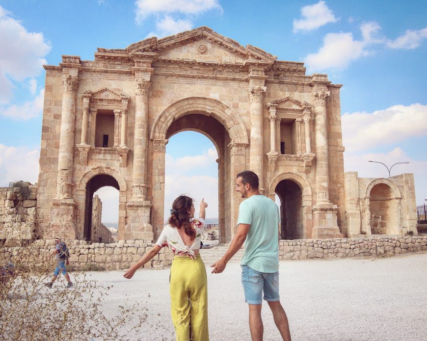 A couple points to an ancient Roman arch at the archeological site of Jerash, Jordan, Middle East