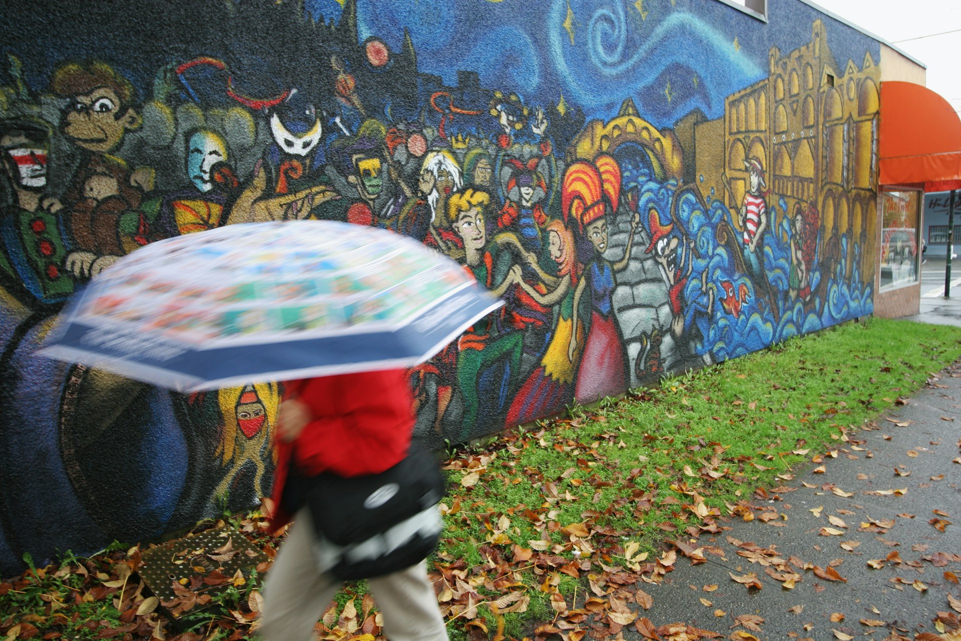 A person holding an umbrella over their head walks by a mural on a wall