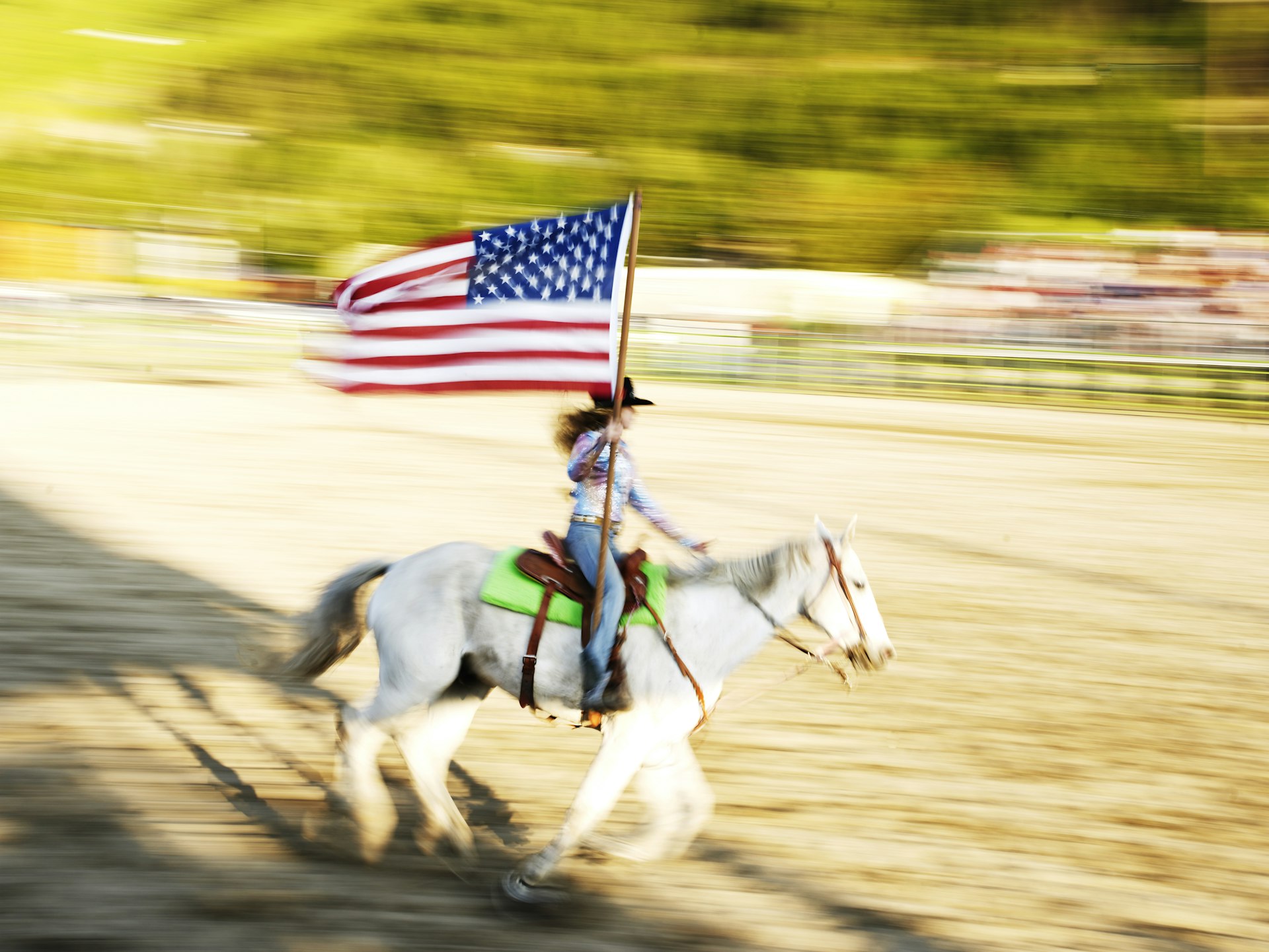 Woman carrying American flag on horseback at rodeo