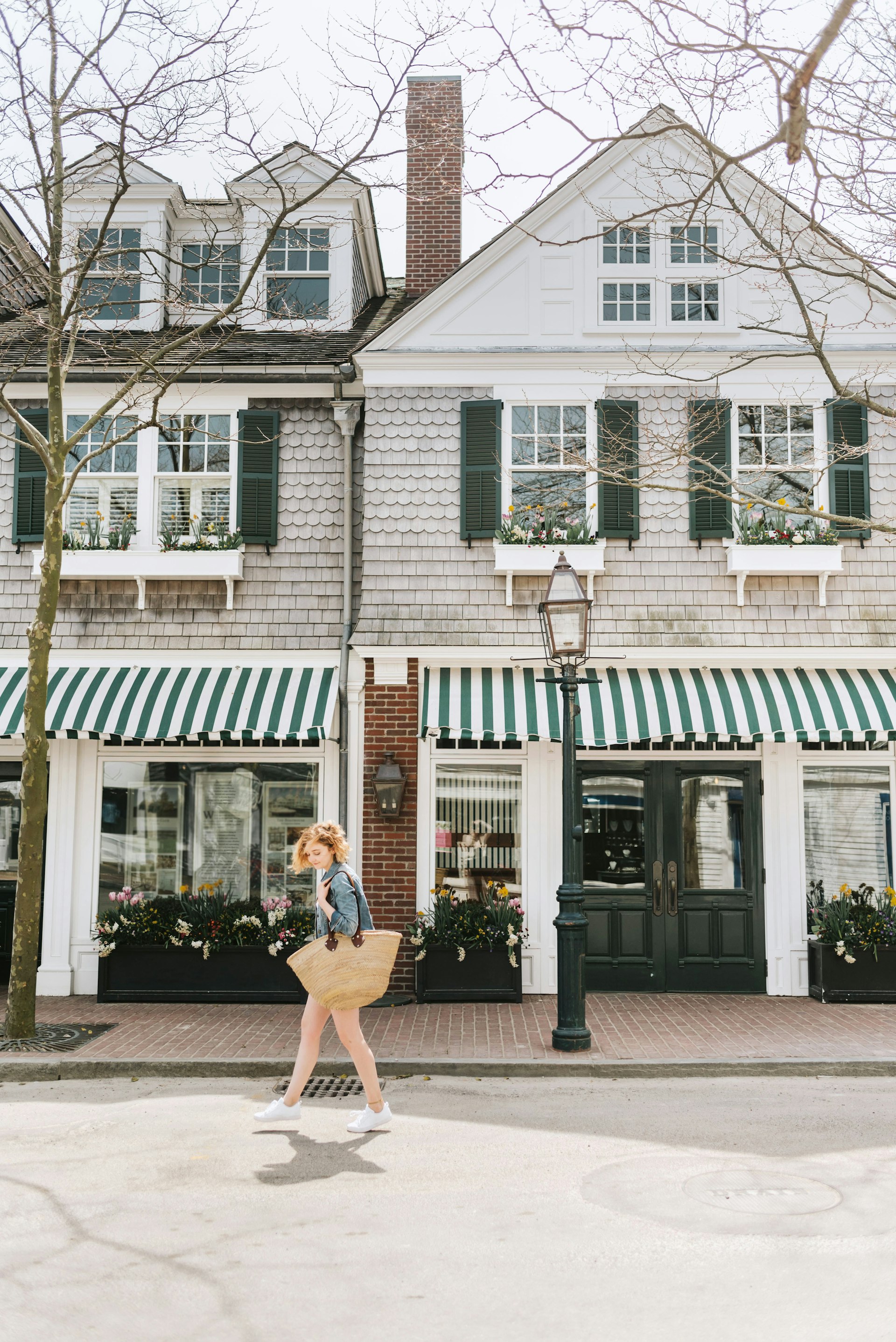A woman carrying a large straw bag walks past a store with a striped green and white awning in Martha's Vineyard. 