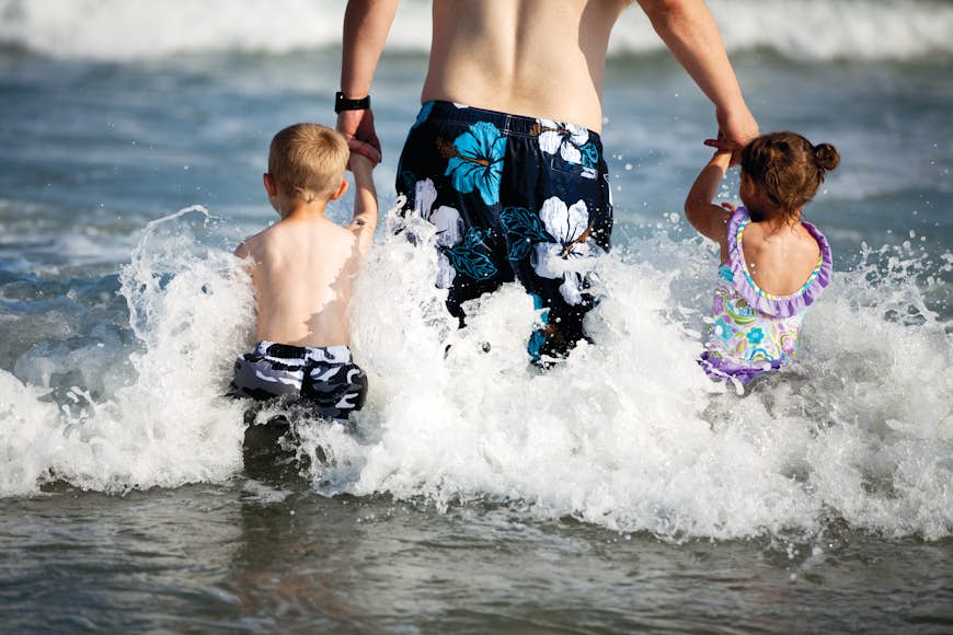 A father and a little boy and little girl head into the water at Myrtle Beach, South Carolina