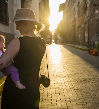 A woman holds a baby as she walks down a cobbled stone street in Panama City. 