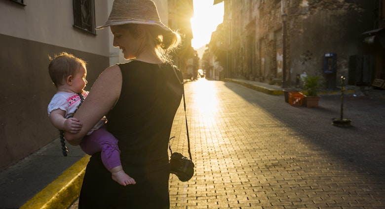 A woman holds a baby as she walks down a cobbled stone street in Panama City. 
