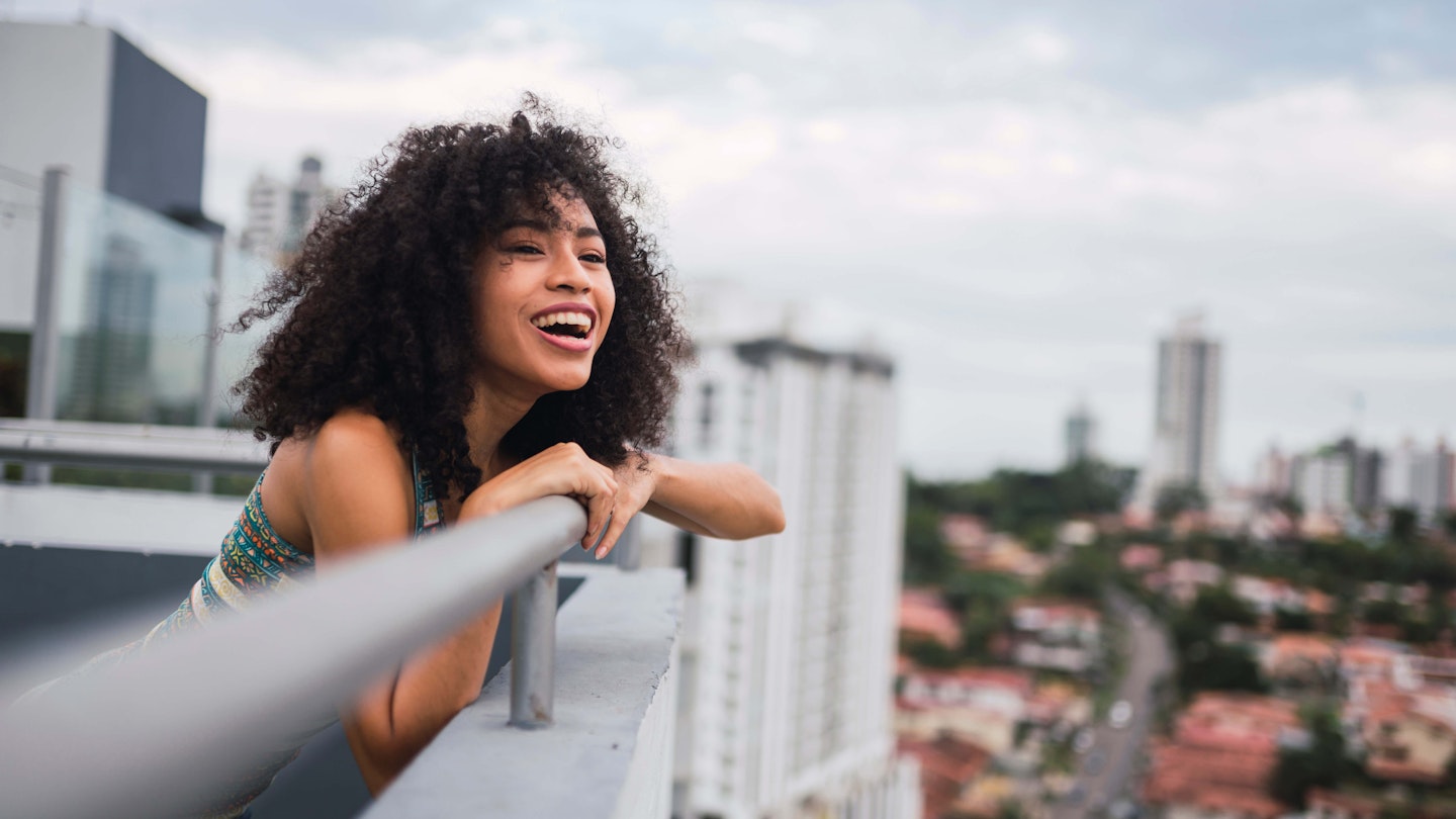 Panama, Panama City, portrait of happy young woman on balcony - stock photo