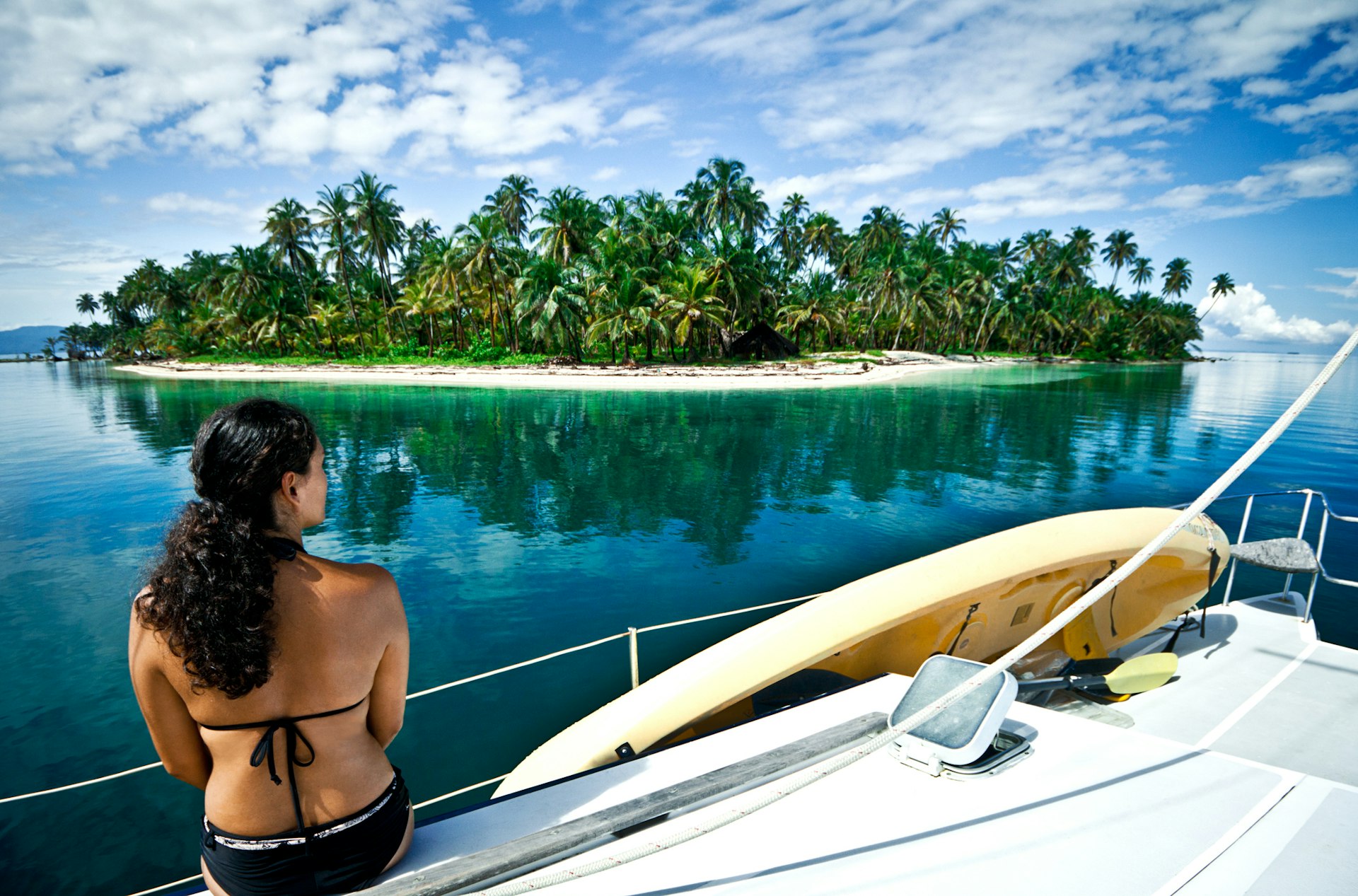 Woman sat on the edge of a boat looking towards an idyllic island